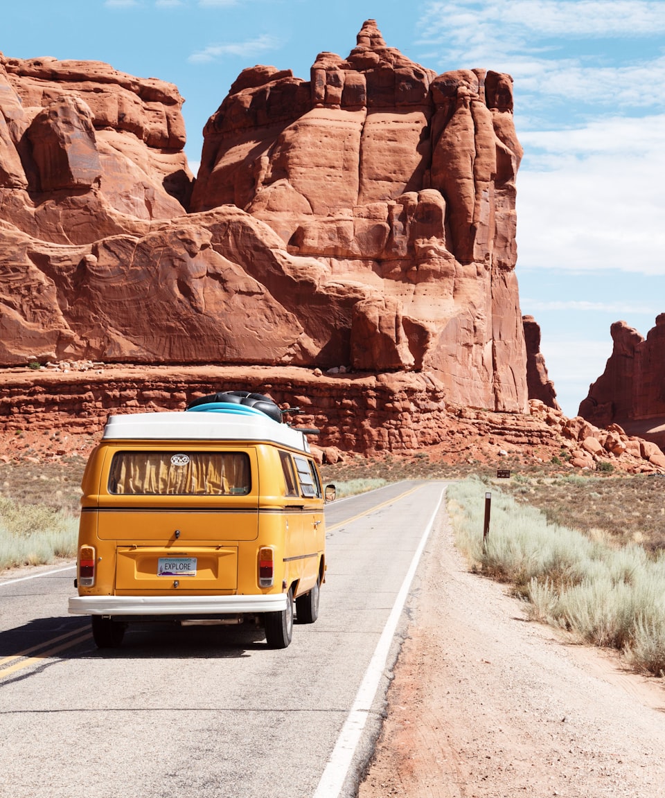 Yellow van driving down a desert road toward red rock formations