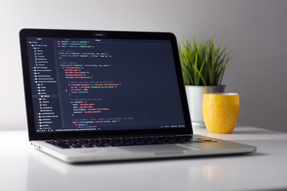 Laptop with a code editor open beside a plant